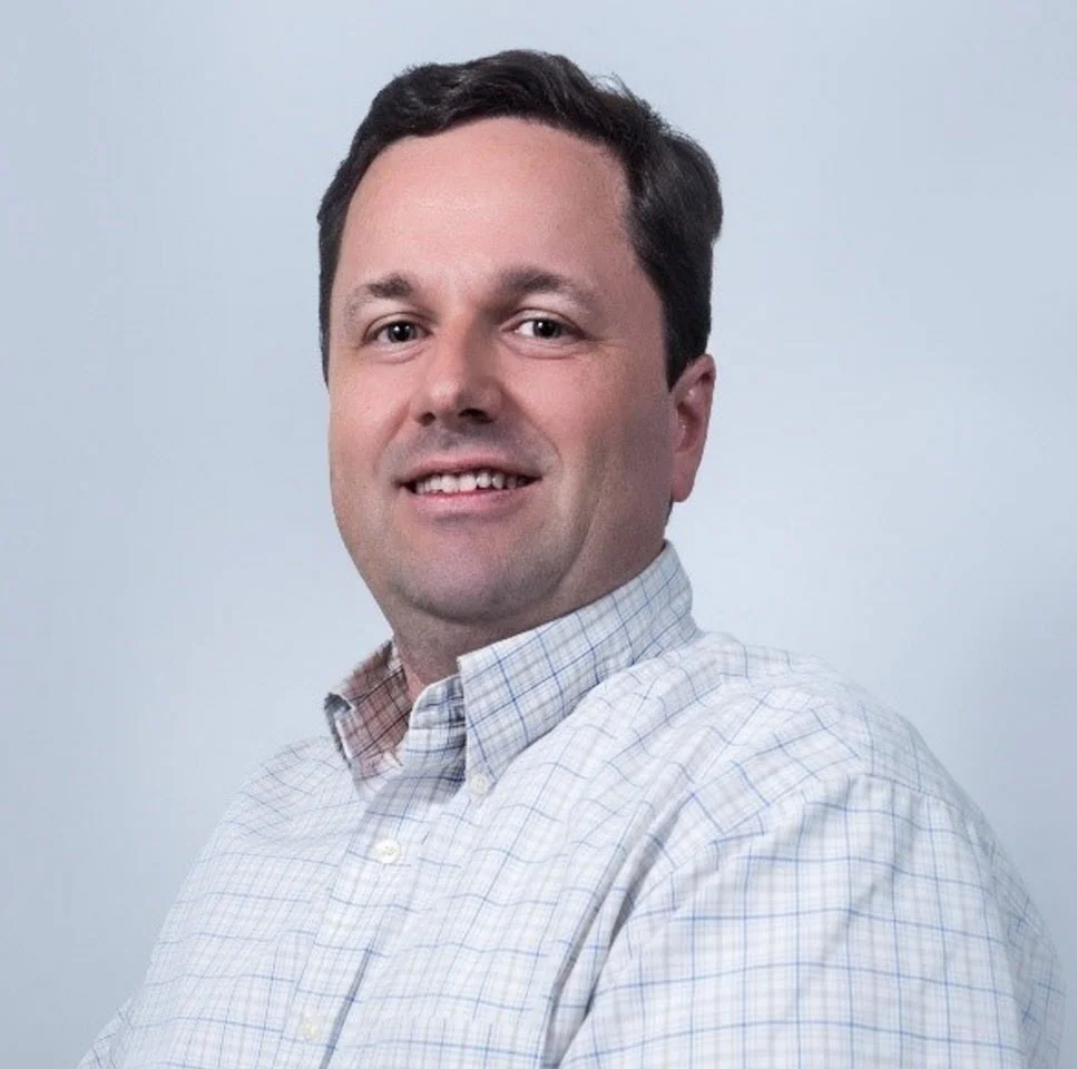 a man in a plaid shirt smiling at the camera